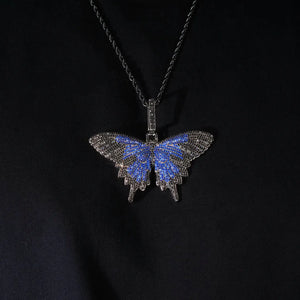 Micro‑pave iced out blue black butterfly pendant necklace black gunmetal tone paired with black twisted rope chain high angle flat lay studio shot full paved VVS simulated diamonds hip hop bling pendant on black fabric background RDRIP JEWELRY
