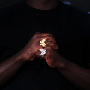 Model wearing two oversized 3D butterfly iced rings gold plated and silver finish full micro pave baguette aaa cubic zirconia mens hip hop bling jewelry lifestyle hand wear shot black outfit dark background RDRIP JEWELRY
