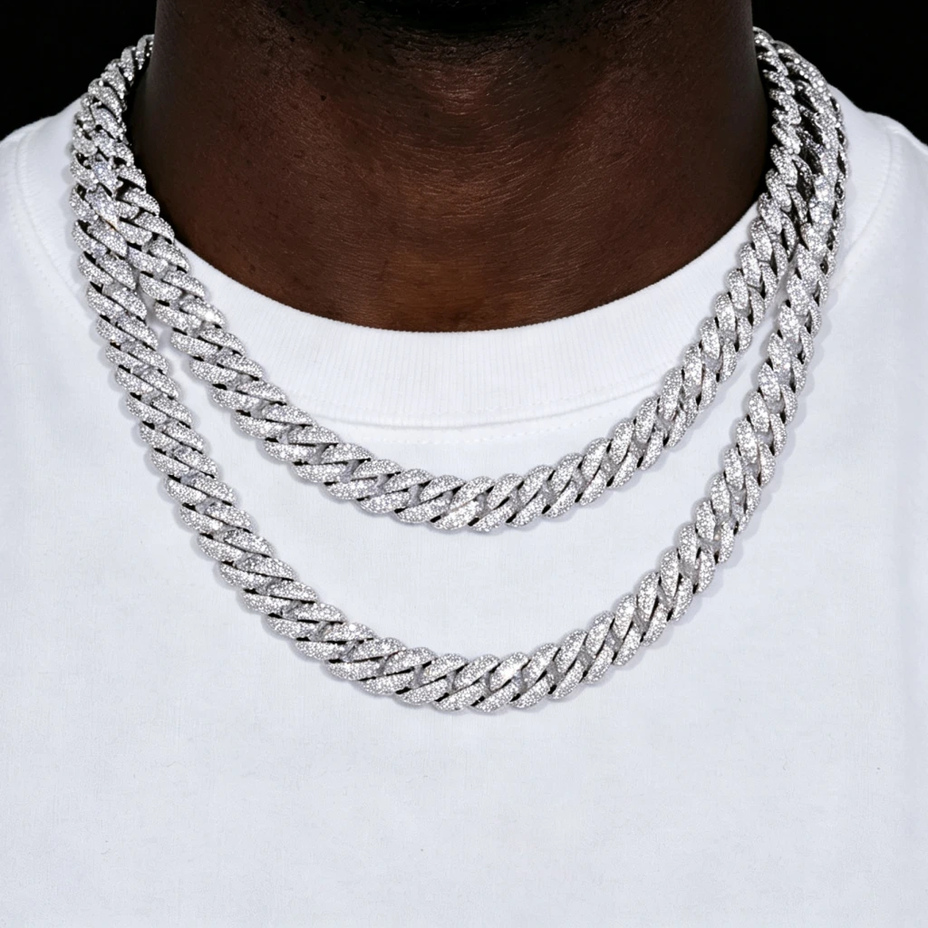 Close up shot of two layered stacked full iced out cuban link chains in 6mm and 10mm width, worn on dark deep black skin hip hop male model with plain white crew neck t-shirt, solid pure black background backdrop, fully encrusted flawless VVS grade simulated diamond stones, 18K white gold plated stainless steel heavy men statement necklace, hand prong set bling flood ice hip hop streetwear jewelry, shiny reflective diamond cuban link chain for men hip hop fashion outfit shot from RDRIP JEWELRY
