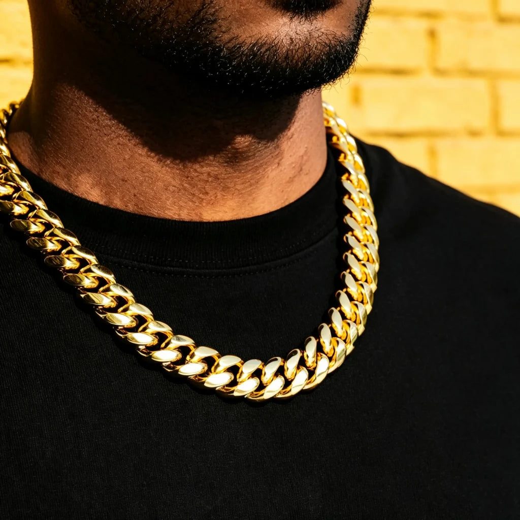 Close-up shot of men wearing chunky 18mm yellow gold plated Miami Cuban link choker necklace, heavy thick polished curb chain hip hop streetwear jewelry, short trimmed beard, clean solid black plain tee, warm yellow brick wall background, shiny reflective gold finish oversized statement Cuban chain for men, tight interlocking links box clasp heavyweight stacking necklace, luxury street hip-hop accessory daily wear layering chain RDRIP JEWELRY since 2016

