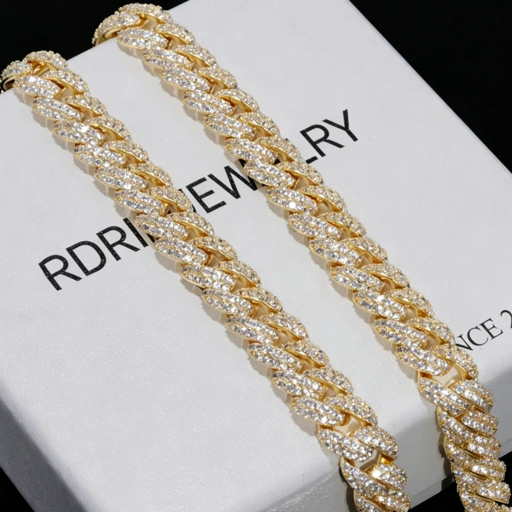 Extreme close-up shot of two 10mm full iced out gold cuban link chains fully encrusted with flawless VVS simulated diamond stones, laid on white branded jewelry box printed RDRIP JEWELRY SINCE 2016, solid pure black background, 18K gold plated heavy hip hop men statement necklace, hand prong set flood ice bling cuban chain luxury gift packaging close up display, shiny reflective diamond hip hop streetwear jewelry gift for men from RDRIP JEWELRY
