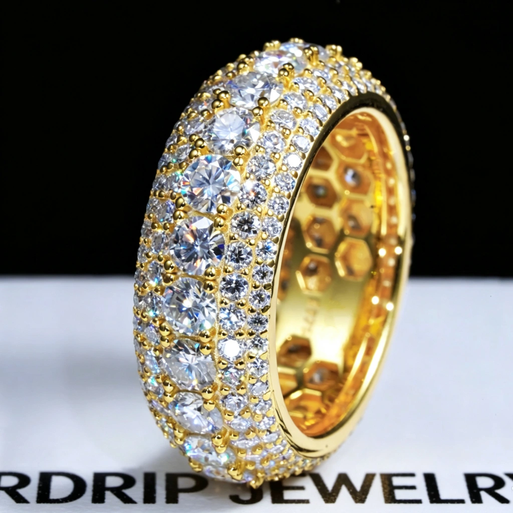 Angled close‑up macro view of men’s hip‑hop 9mm wide multi‑layer full pave moissanite eternity band RDRIP JEWELRY SINCE 2016, 18K gold plated 925 sterling silver ring hand‑set with large 4mm D‑Color VVS1 hearts and arrows round moissanite stones, gold bead prong detailing, inner honeycomb hollow‑cut construction, ring resting on white branded RDRIP JEWELRY paper against solid dark black backdrop, luxury bling statement mens jewelry
