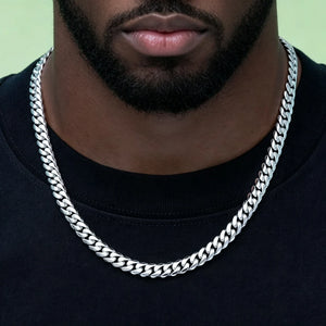 Close-up shot of thick lips black man with neatly trimmed short beard wearing 8mm Flagship Miami Cuban Link Chain in White Gold Tone, polished tight interlock stainless steel men curb necklace, soft light green solid background, anti-tarnish no fade hip hop streetwear jewelry for everyday layering, signature branded clasp, available lengths 16/18/20/22/24 inch shiny icy silver toned cuban link men fashion accessory, heavy durable stackable hip hop chain gift set with dust bag box and lifetime warranty RDRIP