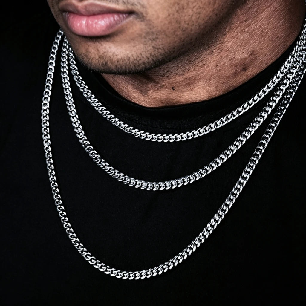 Extreme close-up studio portrait with solid pure black background, male model partial face shot focusing on lips and neck stacked with three 5mm 18k white gold Miami Cuban link chains, multi-length stackable cuban necklace set for men hip hop streetwear, smooth fully polished uniform tangle-free flexible links, premium white gold plated anti-tarnish long-lasting shiny urban men’s statement bling, versatile design to wear alone or match custom hip hop pendants, hand-polished handcrafted artisan cuban jewelry