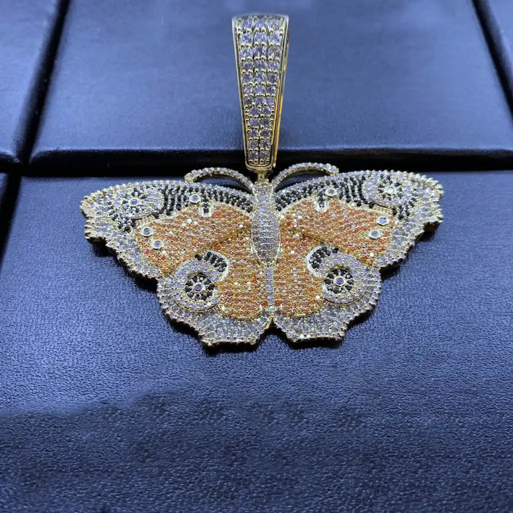 Colorful Iced Out Vintage Butterfly Pendant real item closeup photograph laid on black leather surface, multi‑tone orange black white micro pave AAA cubic zirconia, gold plated hip hop bling charm pendant, detailed insect wing pattern street jewelry for men women RDRIP JEWELRY SINCE 2016
