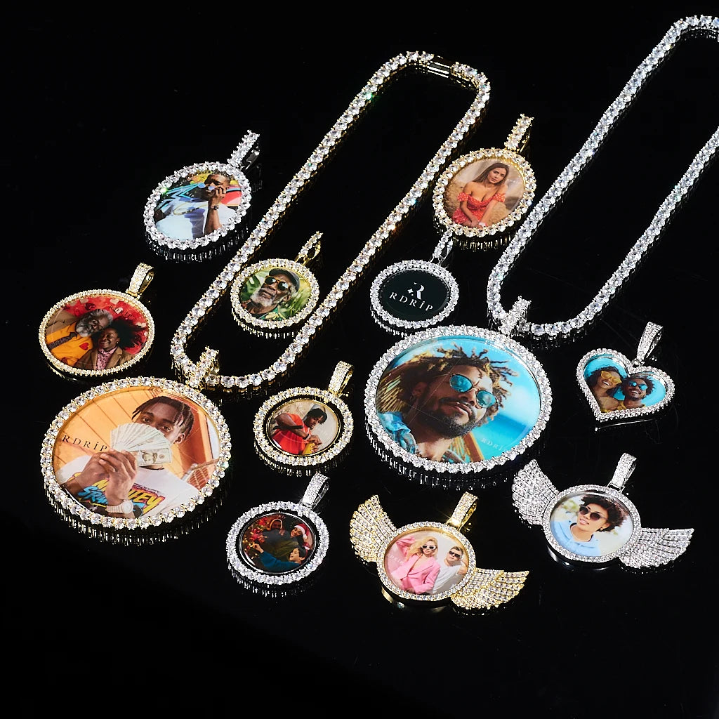 Collection display of CUSTOMIZED photo pendants, mix of round, heart, winged 3D Angle Wing Custom Picture Pendant in gold & white gold with iced tennis chains, personalized hip hop custom memory jewelry flat lay on black background, RDRIP Jewelry
