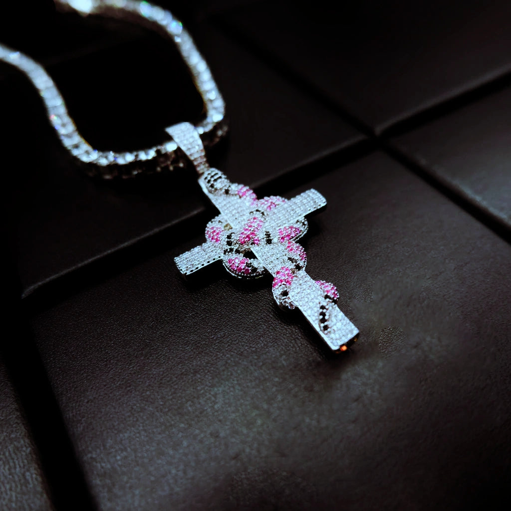 diagonal angle shot silver tone iced out coral snake wrapped cross pendant with bling tennis chain micro‑set pink black cubic zirconia serpent cross hip hop men necklace shot on dark leather background streetwear jewelry RDRIP JEWELRY
