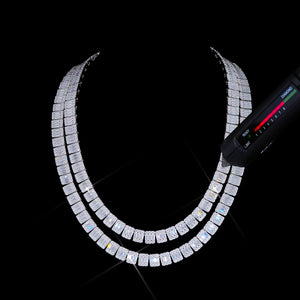 Studio black background shot of double layered 8MM rectangular baguette VVS1+ D color moissanite tennis link chain being tested with handheld cuboid diamond tester pen, tester light indicator turns green to confirm genuine moissanite, solid S925 sterling silver white gold finish, square cluster links with center baguette stones surrounded by round accent moissanite, bright rainbow fire and high light refraction, 9.25 Mohs hardness, superior brilliance compared to cubic zirconia and fake diamond simulants