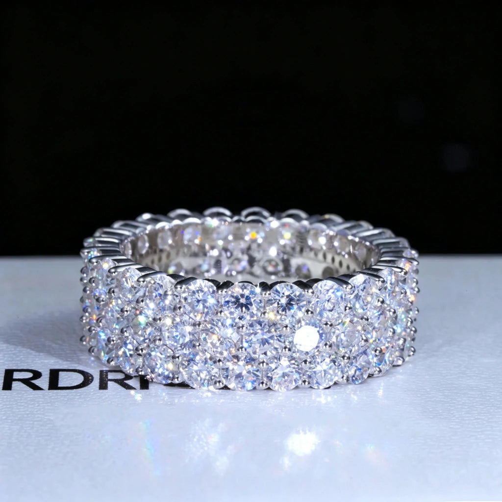 Front view shot of iced‑out 3‑row cluster eternity ring, D‑color VVS1+ hearts and arrows moissanite gemstones hand‑set onto genuine 925 sterling silver white gold plated band, brilliant rainbow light sparkle and fire effect, hip‑hop unisex men bling statement jewelry piece displayed on RDRIP JEWELRY branded gift box surface against dark black background, luxury full eternity wedding band RDRIP JEWELRY
