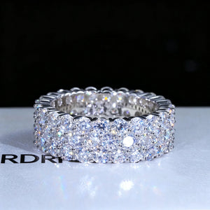Front view shot of iced‑out 3‑row cluster eternity ring, D‑color VVS1+ hearts and arrows moissanite gemstones hand‑set onto genuine 925 sterling silver white gold plated band, brilliant rainbow light sparkle and fire effect, hip‑hop unisex men bling statement jewelry piece displayed on RDRIP JEWELRY branded gift box surface against dark black background, luxury full eternity wedding band RDRIP JEWELRY
