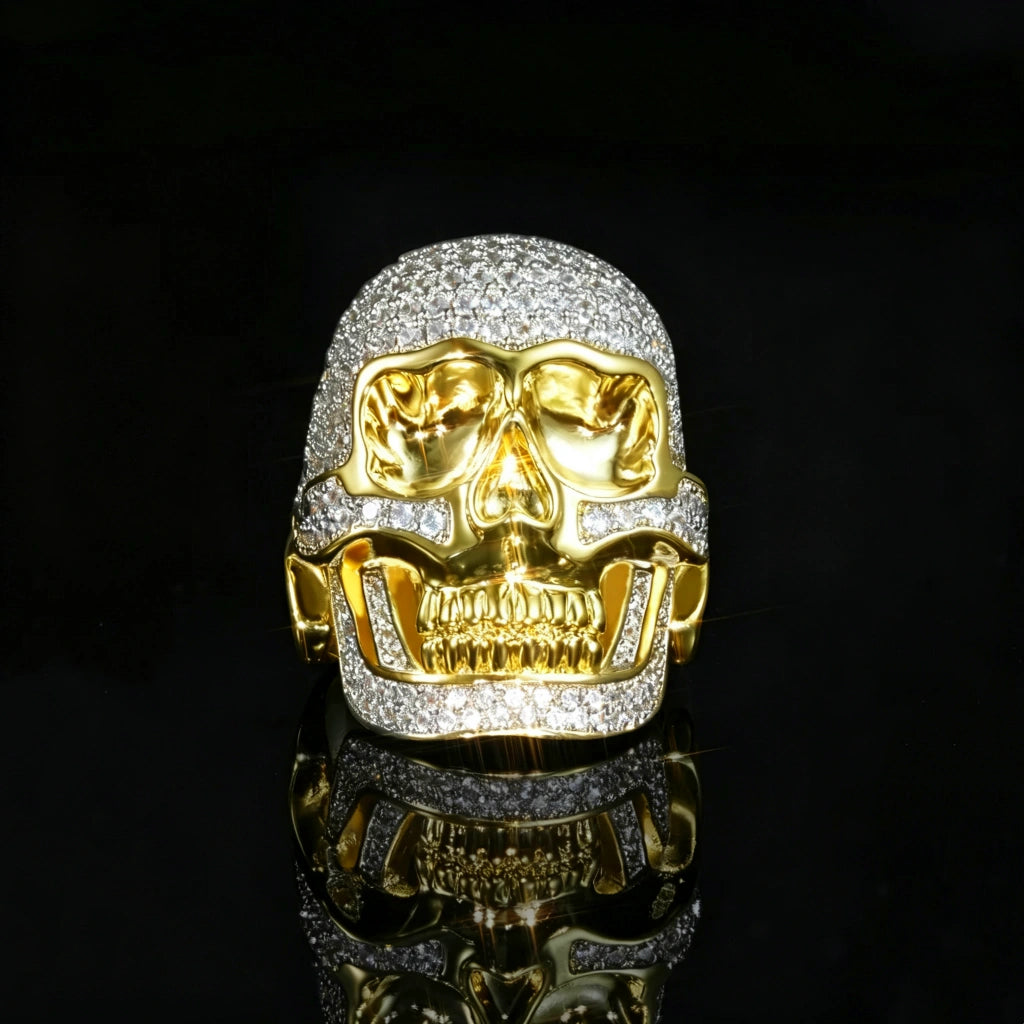 Front close up view two tone 3D iced out skull ring for men, micro pave clear cubic zirconia stones, polished 18k gold plated copper, heavy hip hop statement ring shot on black reflective surface RDRIP JEWELRY
