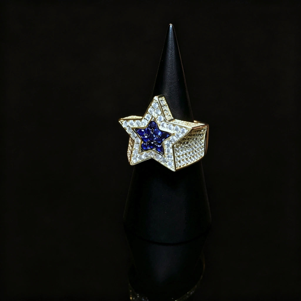 Men’s gold plated iced out double pentagram star hip‑hop ring displayed on black cone ring stand, hand‑set AAA white cubic zirconia surrounding vivid deep‑blue CZ star center, heavy wide micro pave band bling statement ring, premium rap streetwear jewelry piece for men party and gift giving from RDRIP JEWELRY
