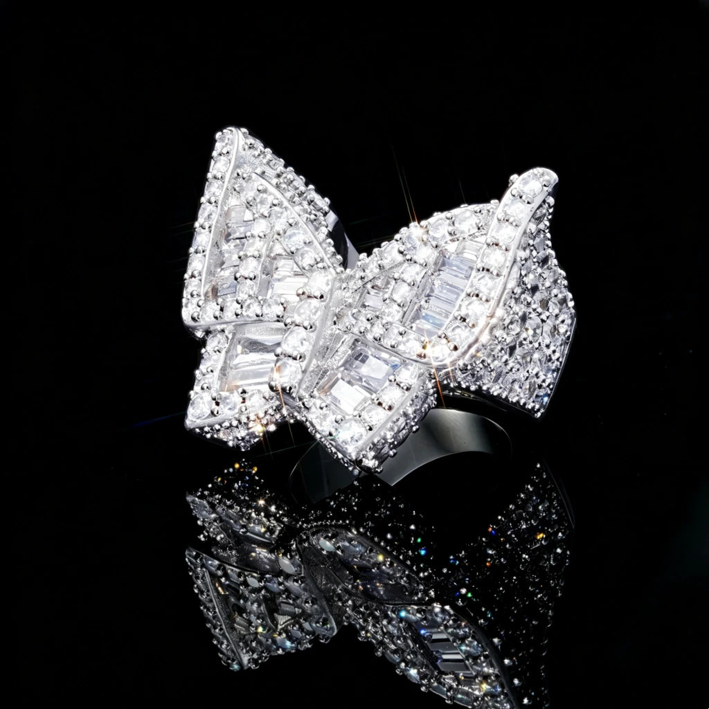 Silver finish iced out baguette butterfly ring angled side view shot, heavyweight 3D hip hop men statement ring, densely hand‑set baguette cut and round cubic zirconia rhinestone gemstones, brilliant sparkling bling diamond‑simulated hip‑hop fashion jewelry, lens flare star‑burst sparkle on black reflective mirror background RDRIP JEWELRY
