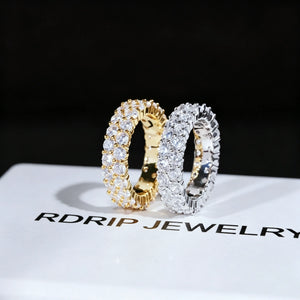 ```
RDRIP JEWELRY iced out double row eternity band gold silver pair resting on branded white gift box prong‑set 3mm round VVS simulated diamonds full iced hip hop mens stackable ring 6mm width copper base bling jewelry dark background studio product close‑up shot