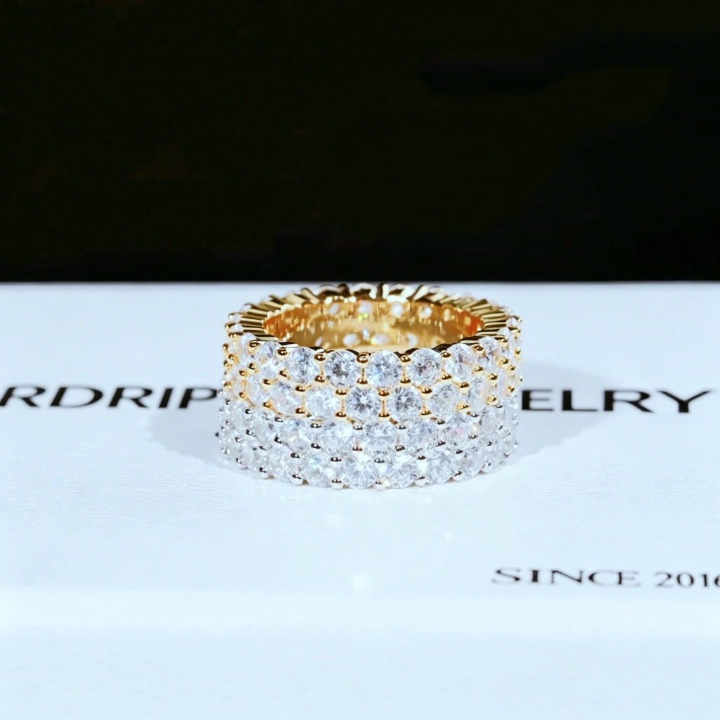 RDRIP JEWELRY iced out double row eternity band single gold tone ring placed on white branded gift box printed SINCE 2016 prong‑set 3mm round VVS simulated diamonds full iced hip hop mens wide stackable ring 6mm width copper base bling jewelry front view studio product close‑up dark blurred background
