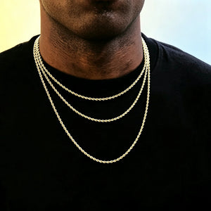 Medium full studio shot of African American male model with ultra short clean skin stubble beard, wearing three different length stackable 2mm 18k gold plated twisted rope chain layered necklaces, slim dainty twisted link staple jewelry for hip hop streetwear men, minimalist unisex gold chain that can be worn alone or matched with custom brand pendants, hand-finished anti-tarnish long-lasting shiny rope chain, smooth soft pale yellow and light blue gradient solid background, clean commercial product 
