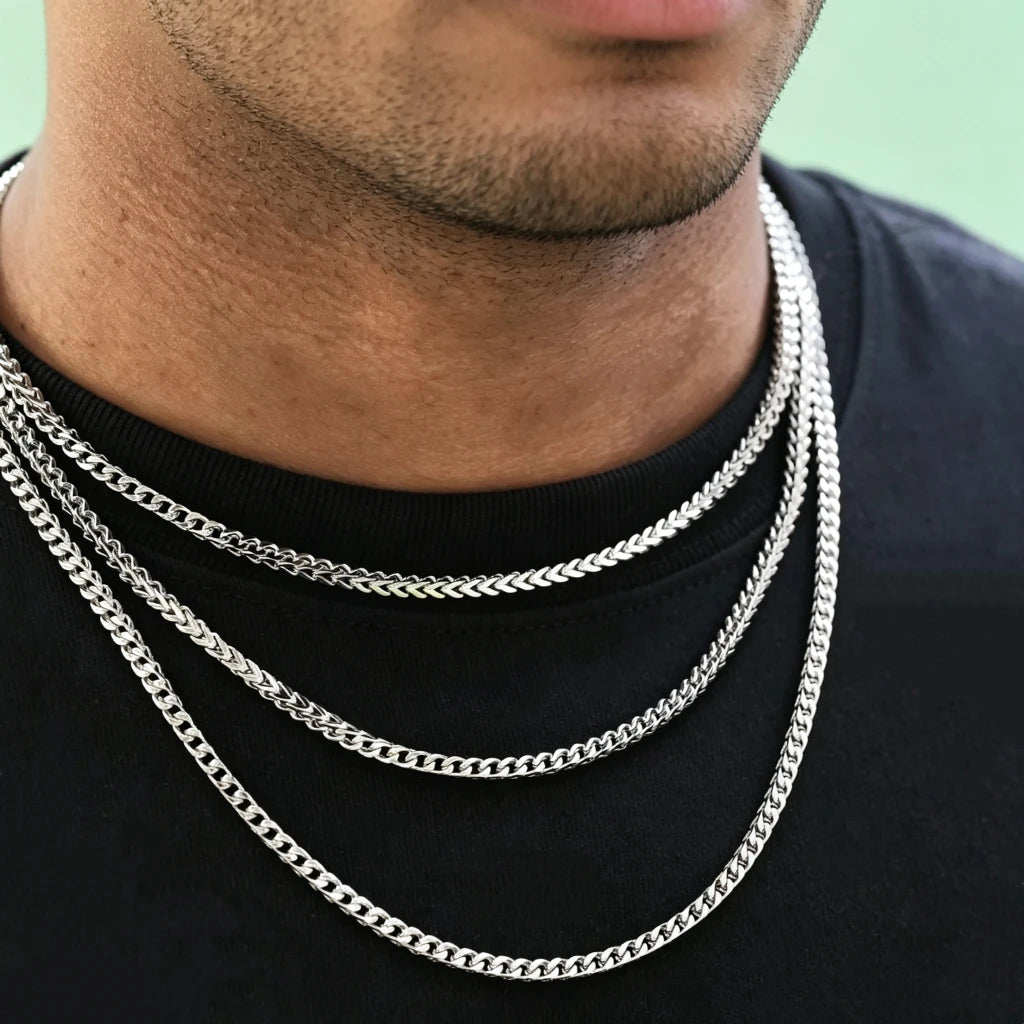 Neck closeup shot of Black male model with ultra-short trimmed stubble beard, wearing three layered stackable polished 3mm white gold Italian Franco link chain necklaces, flexible tangle-free Franco curb chain for men hip hop streetwear fashion, premium anti-tarnish stainless steel unisex minimalist layering jewelry, sleek thin hand-polished Franco chain available in 18 inch and 20 inch lengths, lightweight shiny everyday wearable statement necklace, can be worn solo or matched with custom hip hop pendants