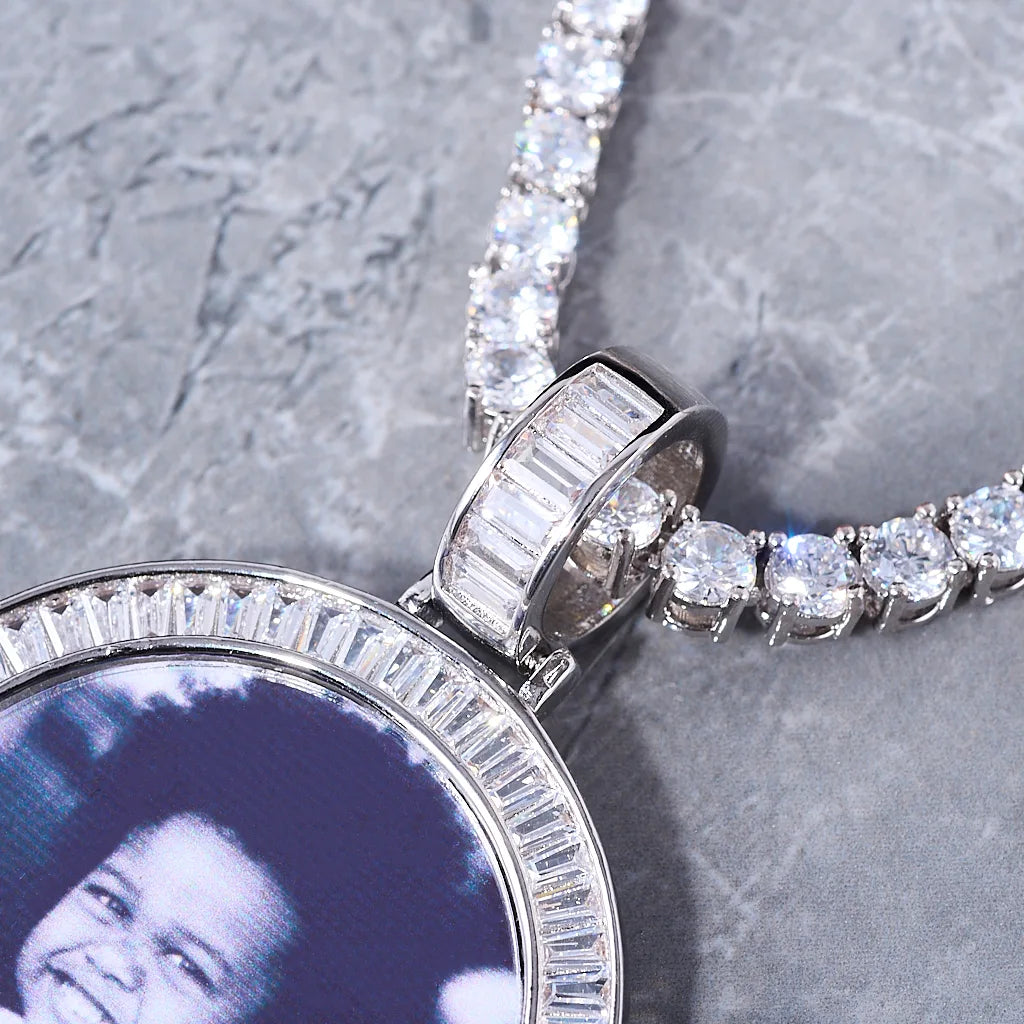 Baguette Iced Out Round Custom Photo Pendant Necklace, close-up detail shot of white gold pendant. Features hand-set baguette stones on the bail and circular frame, custom child portrait photo, tennis chain laid on grey marble texture surface, personalized hip hop custom jewelry, RDRIP JEWELRY
