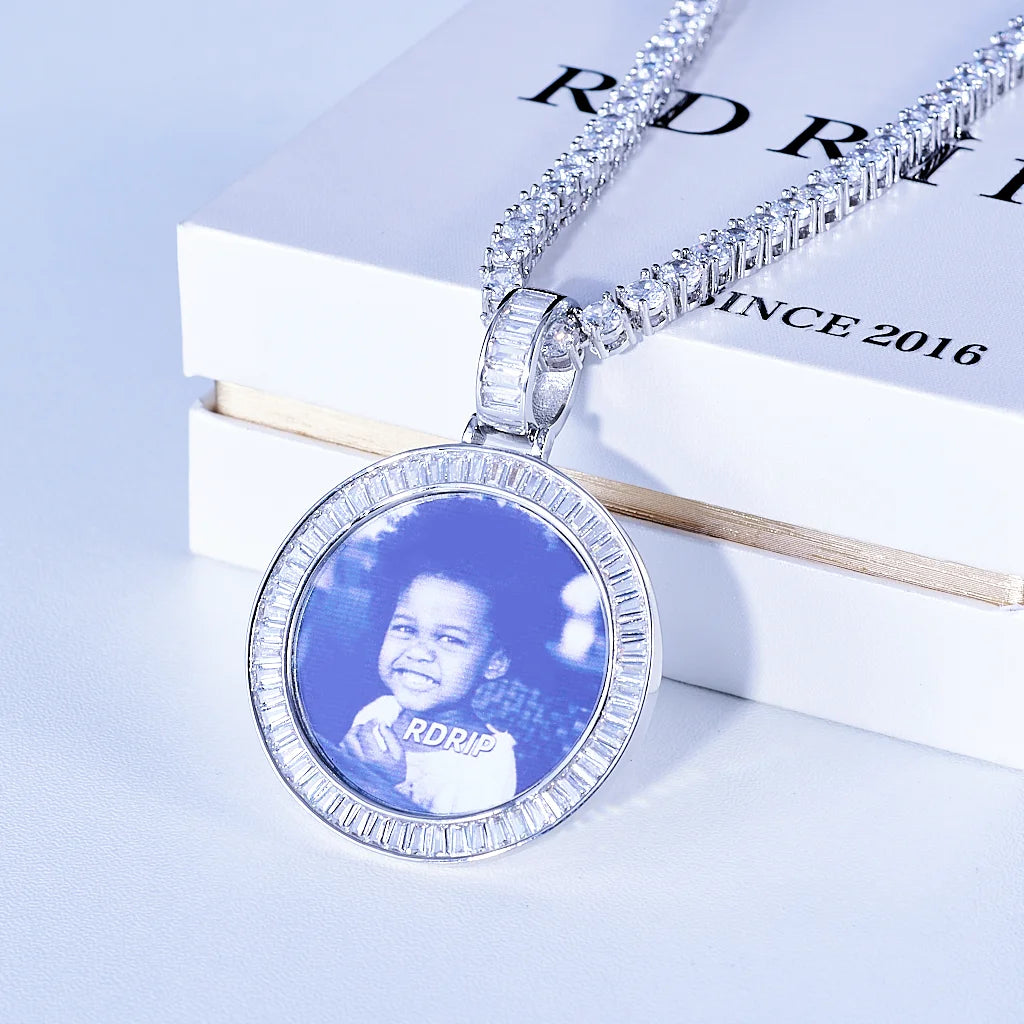 Baguette Iced Out Round Custom Photo Pendant Necklace, white gold tone pendant with baguette-cut stone frame, custom child portrait photo with glass surface reflection, tennis chain placed on official RDRIP branded white gift box, light background commercial product shot, personalized hip hop keepsake jewelry, RDRIP JEWELRY
