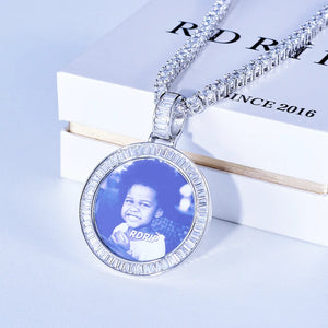 Baguette Iced Out Round Custom Photo Pendant Necklace, white gold tone pendant with baguette-cut stone frame, custom child portrait photo with glass surface reflection, tennis chain placed on official RDRIP branded white gift box, light background commercial product shot, personalized hip hop keepsake jewelry, RDRIP JEWELRY
