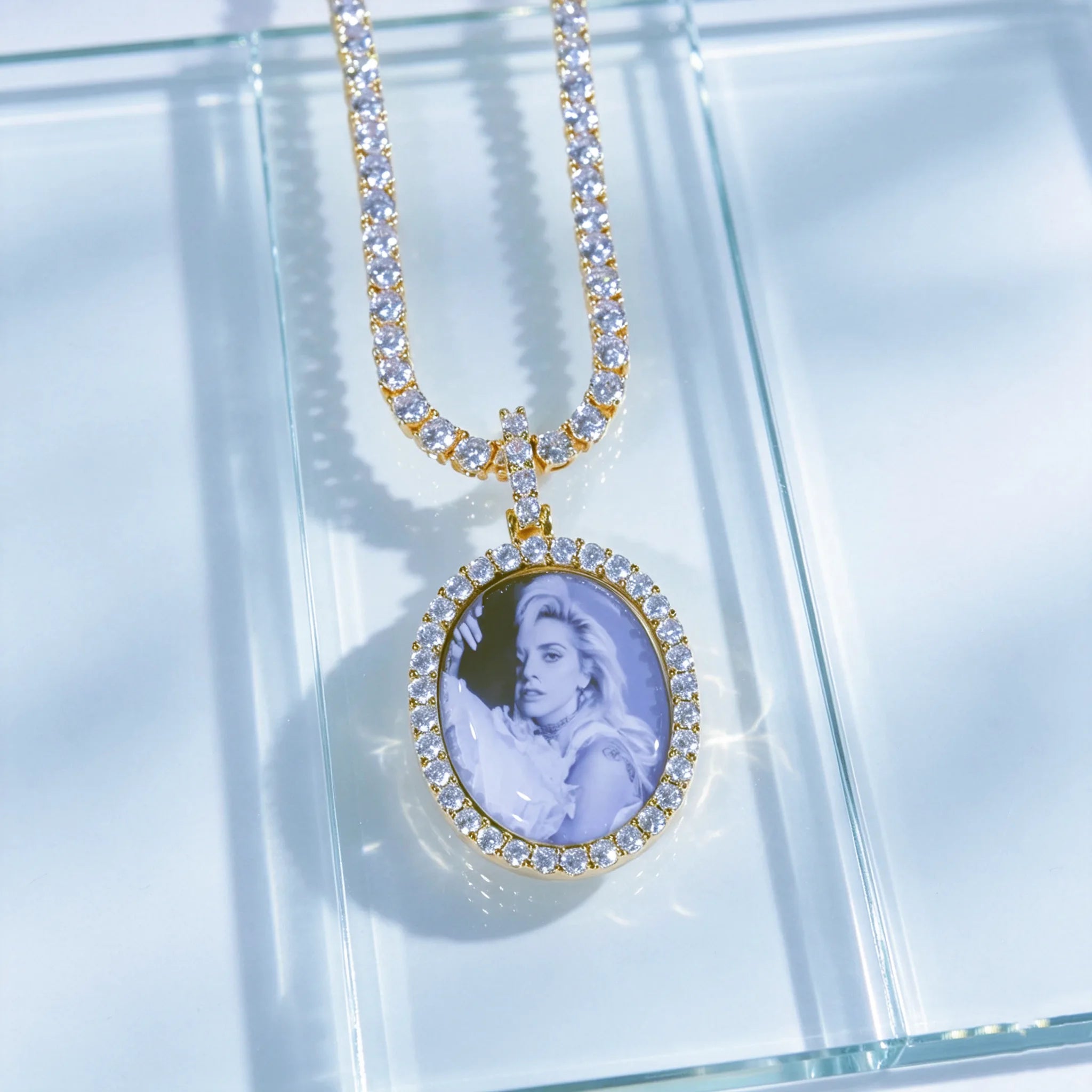 Gold Oval Halo Custom Photo Pendant Necklace with tennis chain, custom printed portrait photo inside oval medallion, laid flat on seamless light clear transparent glass surface, professional studio jewelry photography, RDRIP JEWELRY personalized hip hop memory pendant
