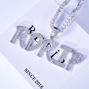 Iced Out Baguette Custom Name Letter Pendant Necklace, white gold tone oblique front view, mixed baguette and round cut stones custom letter pendant spelling RDRIP, tennis chain laid on official RDRIP branded gift box, light studio background, personalized hip hop custom name jewelry, RDRIP JEWELRY

