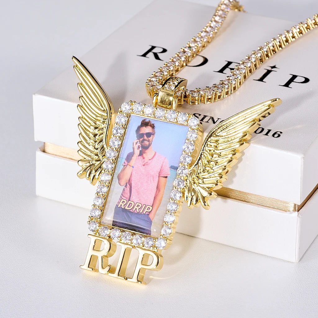 Iced Out Wings RIP Custom Photo Pendant, gold tone oblique front view, angel wing rectangular custom photo frame pendant with RIP letter decoration, encrusted round stones, matched tennis chain laid on official RDRIP branded gift box, light studio background, memorial personalized hip hop keepsake jewelry, RDRIP JEWELRY
