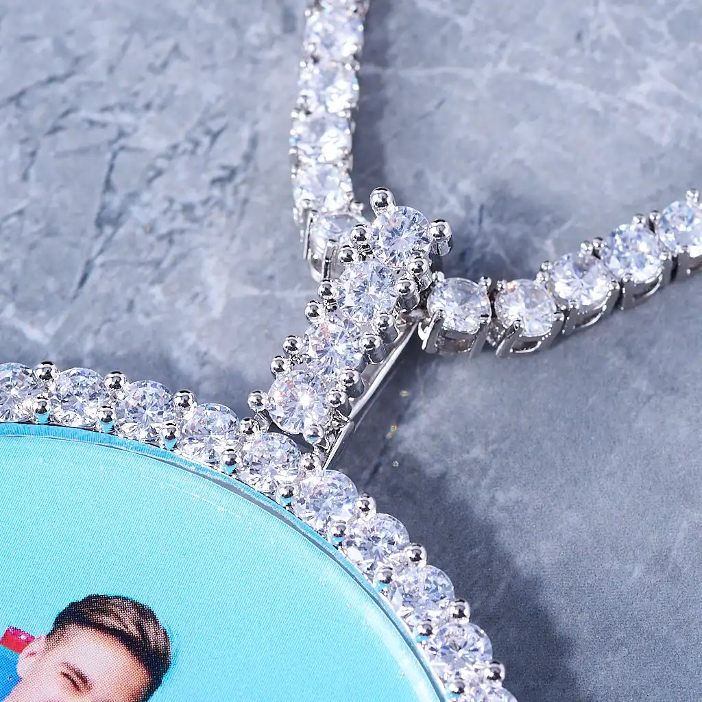 VVS MOISSANITE LARGE 3D CIRCLE CUSTOM PICTURE PENDANT, macro close-up view of silver plated VVS moissanite encrusted bail and stone border frame, matched with iced out tennis chain, premium hip hop jewelry detail shot on grey marble surface, RDRIP JEWELRY
