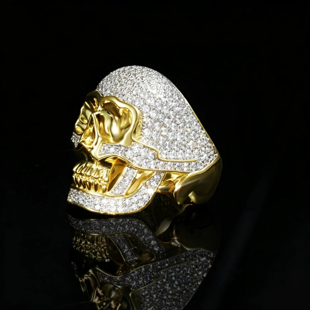 Side profile shot of two tone 3D iced out skull ring for men, full micro pave cubic zirconia setting, polished 18k gold plated copper construction, heavy bulky hip hop bling jewelry on black reflective background RDRIP JEWELRY
