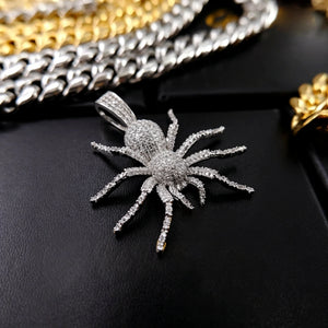 Silver toned Iced Tarantula Spider Pendant flat lay shot, fully micro paved VVS simulated diamonds spider hip hop charm, surrounded by mixed cuban link chains in gold and silver tone on black leather surface, men bling urban streetwear jewelry closeup RDRIP JEWELRY
