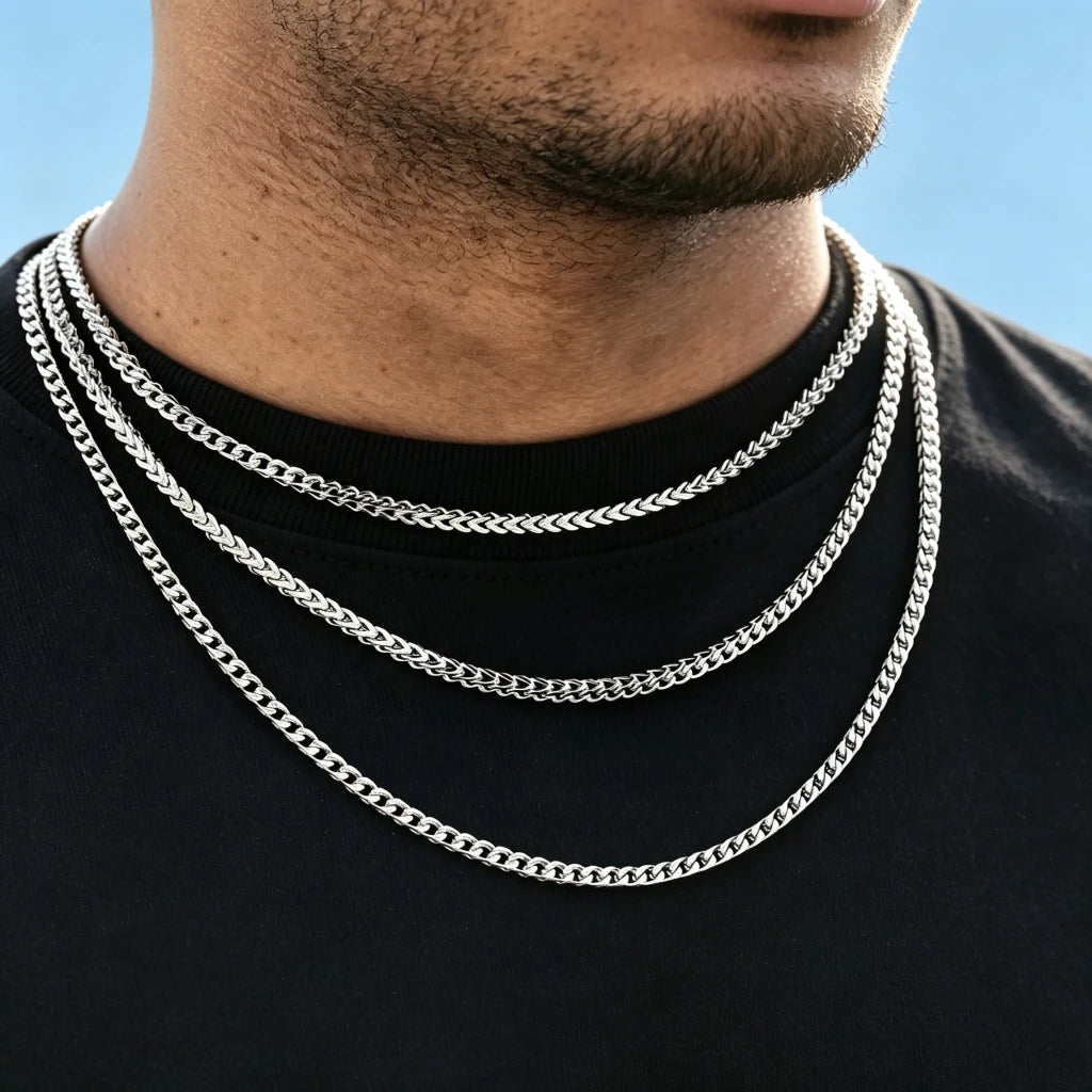 Close up model shot of men wearing three layered stackable 3mm polished white gold Italian Franco link chain necklaces, flexible tangle-free Franco curb chain for hip hop streetwear fashion, solid polished stainless steel unisex minimalist layering jewelry, sleek thin Franco chain available in 18 inch and 20 inch lengths, lightweight anti-tarnish everyday statement necklace perfect for solo wear or matching custom hip hop pendants, clean plain light blue background solid black tee, no dust or skin flake ble