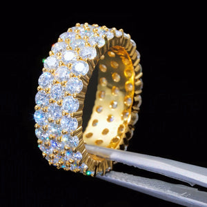 18K gold plated genuine 925 sterling silver 3 row cluster moissanite eternity ring held by precision tweezers against solid black background, hand‑set D‑color VVS1 plus 4mm round hearts and arrows moissanite stones, 8mm wide iced‑out full band hip hop unisex ring, showing inner hollow hole details, brilliant light refraction and icy sparkle, GRA certified moissanite jewelry for men women RDRIP JEWELRY
