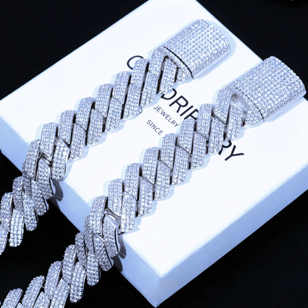 Flat lay studio product shot featuring two 19mm wide full iced out prong cuban link bracelets resting on branded RDRIP JEWELRY gift box printed with SINCE 2016, every cuban link and large box clasp fully covered with flawless lab tested VVS simulated diamonds set by skilled hand prong lifting craftsmanship, solid copper base coated with premium shiny 18K white gold plating, heavy oversized unisex hip hop bling wrist jewelry with brilliant icy reflective shine, tarnish and scratch resistant luxury streetwear