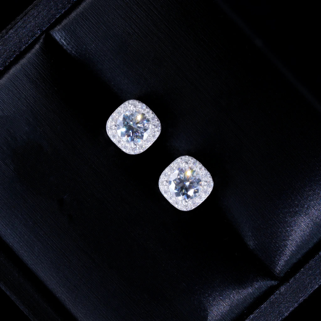 VVS1 Moissanite 7MM Cushion Halo Stud Earrings, 925 sterling silver white gold plated screw‑back unisex hip‑hop studs, round center VVS1 moissanite surrounded by pave cushion halo frame, vivid fire dispersion and bright starburst sparkles, angled close‑up shot of earrings resting inside luxury black silk‑lined gift box, premium gift ready jewelry presentation, RDRIP JEWELRY
