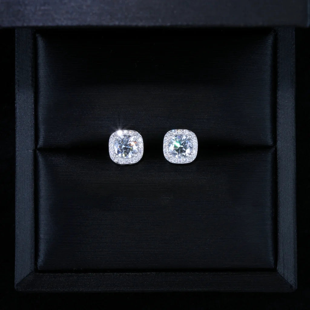 VVS1 Moissanite 7MM Cushion Halo Stud Earrings, 925 sterling silver white gold plated screw‑back unisex hip hop studs, round center VVS1 moissanite with pave cushion halo frame, dazzling starburst sparkle and brilliant fire, top‑down overhead product photograph of earrings placed inside luxury black silk‑lined gift box, perfect gift presentation shot, RDRIP JEWELRY
