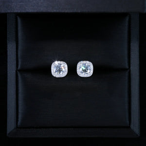 VVS1 Moissanite 7MM Cushion Halo Stud Earrings, 925 sterling silver white gold plated screw‑back unisex hip hop studs, round center VVS1 moissanite with pave cushion halo frame, dazzling starburst sparkle and brilliant fire, top‑down overhead product photograph of earrings placed inside luxury black silk‑lined gift box, perfect gift presentation shot, RDRIP JEWELRY
