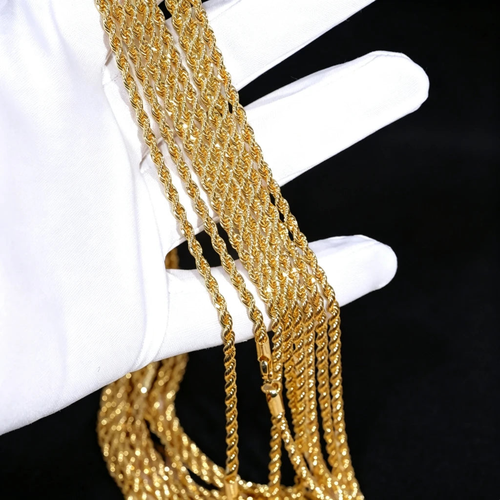 Extreme closeup product photograph of multiple bulk 2mm 18k gold plated twisted rope chains held gently by soft white cotton inspection gloves, slim dainty twist link necklaces with polished shiny gold finish, assorted stackable lengths for men hip hop layering styling, blank chain ready to pair with custom hip hop pendants, anti-tarnish handcrafted unisex streetwear jewelry supply, clean solid pure black background, wholesale jewelry stock shot for rap fashion accessories RDRIP JEWELRY SINCE
