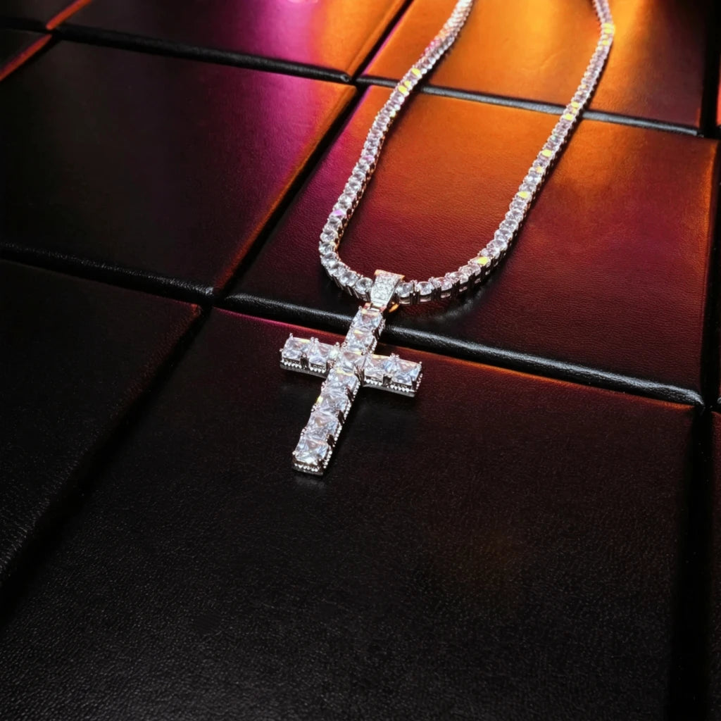 White gold plated baguette cut cross pendant matched with iced tennis chain laid flat on black leather surface, bling vvs simulated diamond hip hop necklace for men street fashion accessory RDRIP JEWELRY
